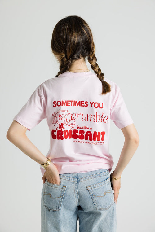 Rückansicht des rosafarbenen T-Shirts mit großem roten Aufdruck: ein Croissant-Charakter und der Text „SOMETIMES YOU crumble just like a CROISSANT and that’s okay, you got this.“